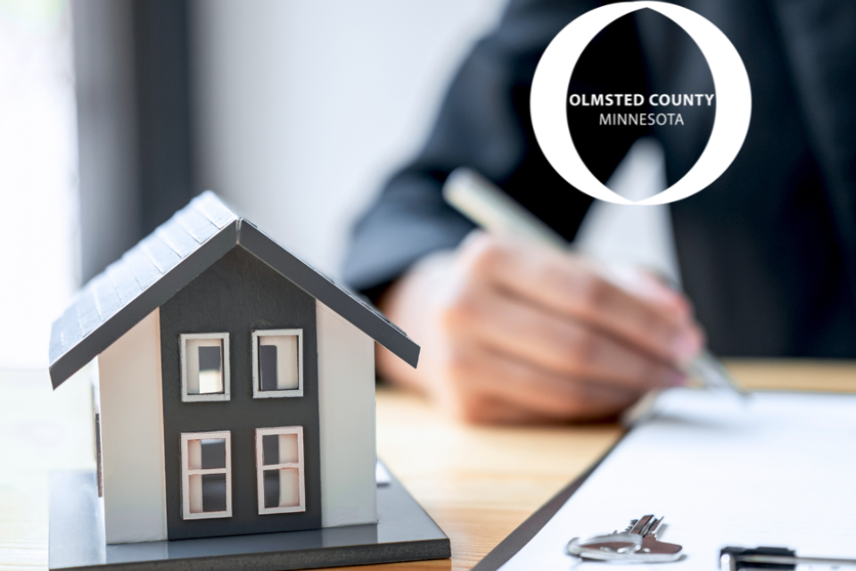 A model home. The Olmsted County logo. A person writing on paper.
